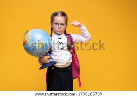 a little girl in school uniform holds a globe in her hands on a yellow background.