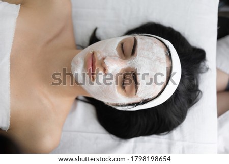 Beautician applying enzymatic peeling on woman's face at spa. Applies a white mask with a brush. Cosmetic procedure in a modern beauty salon