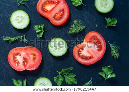 Sliced tomatoes, cucumbers, parsley and dill on a black background