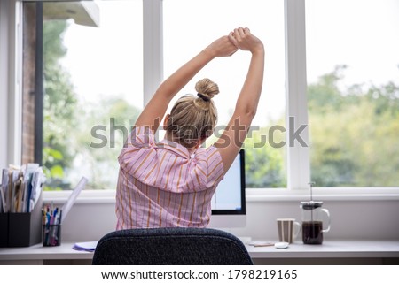 Rear View Of Woman Working From Home On Computer  In Home Office Stretching At Desk Royalty-Free Stock Photo #1798219165