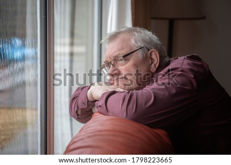 Bored man in sixties looking out the window in home 