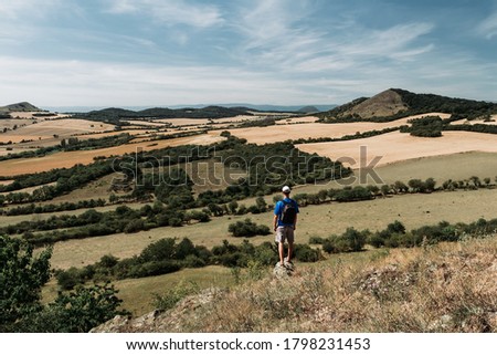 Young man with backpack standing on rock and looking to Czech central mountain valley