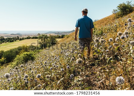 Young man standing in thistle flower and looking to Czech central mountain valley