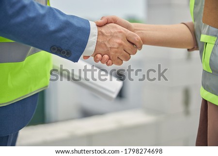 Cropped photo of a Caucasian business lady and an engineer with a drawing greeting each other