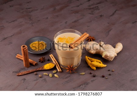 Popular Indian drink  Karak tea or Masala chai. Prepared with the addition of milk, variety of spices and spices. Transparent cup on a brown textured background next to the ingredients. Royalty-Free Stock Photo #1798276807