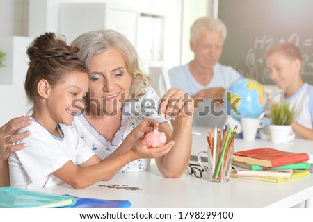 Portrait of grandmother and Child Daughter Putting Coins into Piggy Bank