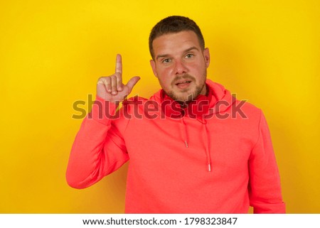 Close up portrait of pleasant looking blue eyed young man model has clever expression, raises one finger, remembers himself not to forget tell important thing.