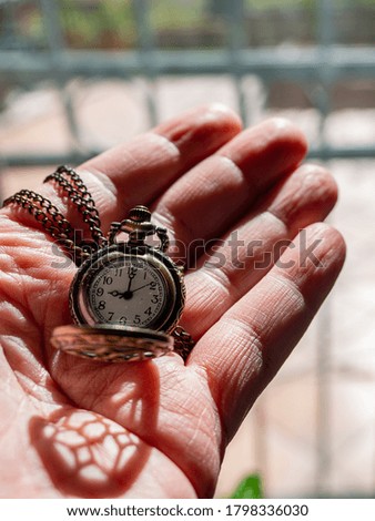Photo of a man hand holding a pocket watch, with a railing in the background