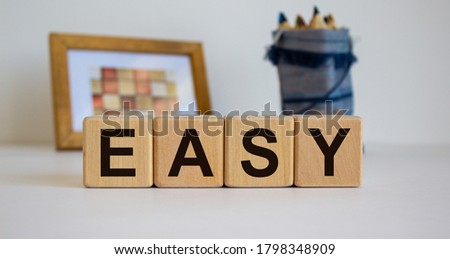 Wooden cubes with the inscription 'easy'. Frame with a picture and a bag with pencils in the background. Concept.