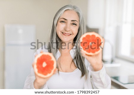 People at home concept. Portrait of smiling retired gray haired woman holding grapefruit slices for breakfast in the kitchen. Healthy food, elderly people concept Royalty-Free Stock Photo #1798392457