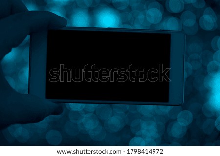 Mockup image of hand holding white mobile phone with blank black  screen. round bokeh background.