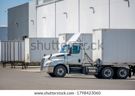 Big rig local haul day cab industrial freight white semi truck with roof spoiler loading commercial cargo in dry van semi trailer standing at the warehouse dock gate in row with another semi trailers Royalty-Free Stock Photo #1798423060
