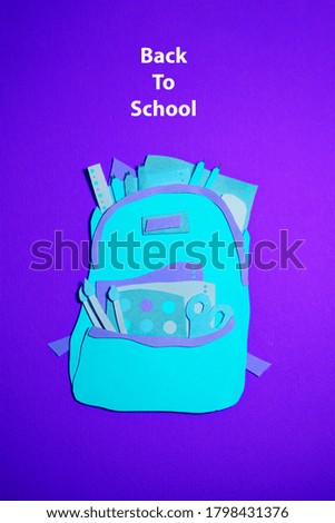 The handmade backpack with school accessories was cut out of blue and purple paper. The vertical photo of the paper art was made for back to school craft design.