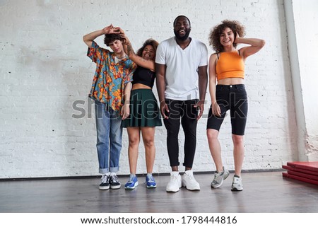 Full length photo of happy four friends standing against white wall and grimacing at camera in studio