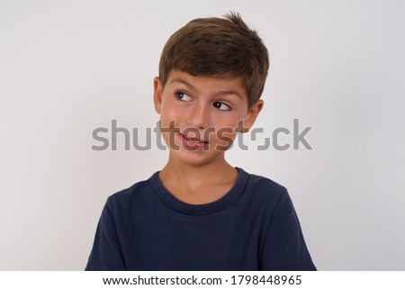 Photo of amazed Beautiful kid boy wearing casual t-shirt standing over isolated white background bitting lip and looking up to empty space, 