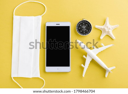 World Tourism Day, Top view of minimal model plane, airplane, starfish, compass, smartphone blank screen and face mask isolated on yellow background, accessory flight holiday under coronavirus concept
