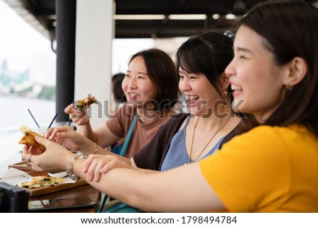 Asian women friends having fun smiling and laughing with drink and snack while going out for cafe hopping relaxing at the cafe with a river view at the background,  girl friendship, sisterhood.