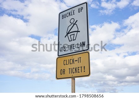 Buckle up sign and 'Click It or Ticket' warning sign against blue sky and clouds.