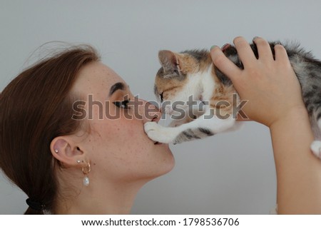The girl holds a kitten in her hands near her face, and they look at each other. A girl with a tricolor kitten in profile. Photo with selective focus.