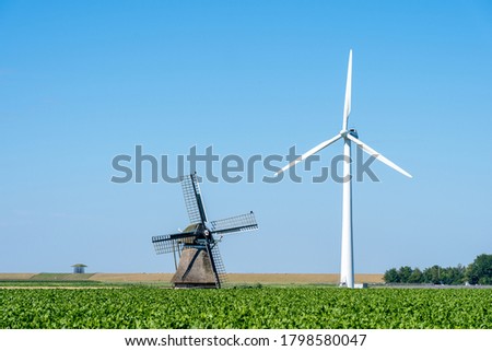 A big contrast in picture: an old traditional windmill among a number of modern wind turbines under a clear blue sky