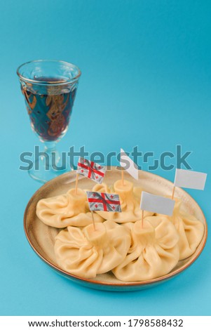 Khinkali cooked on a ceramic plate served with a glass of wine over pastel blue background. Copy space banner. Delicious meat dumplings. Traditional Georgian cuisine. Georgian flag picture.