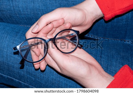 Close-up of human hands holding blue rimmed glasses on their knees. Eyes rest from glasses. Glasses are an accessory
