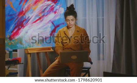 Painter searching inspiration on laptop in art studio.