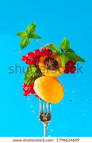 Fresh apricot, red currant and mint on a fork with flowing water drops and splashes on a blue background. Diet healthy food concept. Copy space.