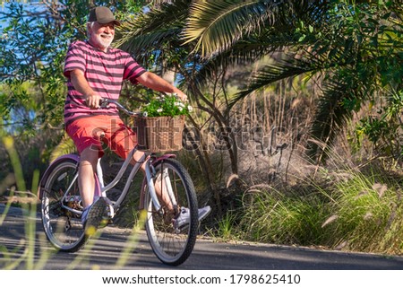 Cheerful senior man with white beard riding with a vintage bicycle enjoying freedom, basket with daisies - concept of active playful elderly during vacation