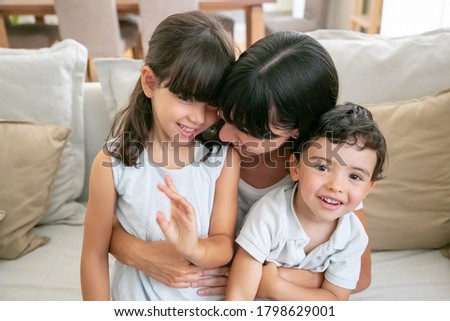 Happy mom enjoying time with kids at home. Cheerful mother and two children sitting on couch in living room together. Leisure time with family concept