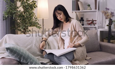 attractive asian woman in casual attire is spending time with herself reading in living room. relaxing female homeowner is engaging in sedentary activity during her downtime in her cozy living room. Royalty-Free Stock Photo #1798631362