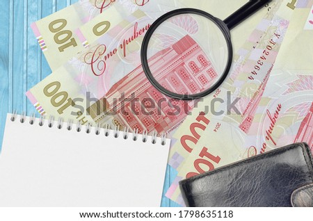 100 Ukrainian hryvnias bills and magnifying glass with black purse and notepad. Concept of counterfeit money. Search for differences in details on money bills to detect fake