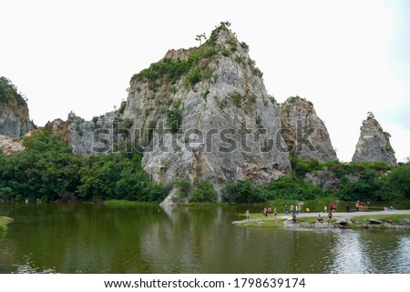 Beautiful range of rocks mountain with many tourists sightseeing around still pond or lake at Kuao Hin Ngu public park in Ratchaburi province, Thailand