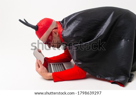 Stylish caucasian man in devil hat with horns and vampire cape with laptop isolated on white backhround.