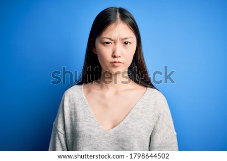 Young beautiful asian woman wearing casual sweater standing over blue isolated background skeptic and nervous, frowning upset because of problem. Negative person.