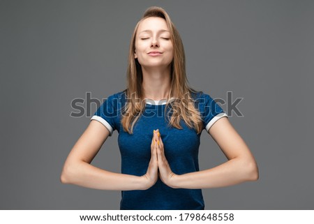 Young blonde woman practicing yoga, holding hands in namaste and keeping her eyes closed. She meditating indoors, praying for peace and love, having calm and peaceful facial expression