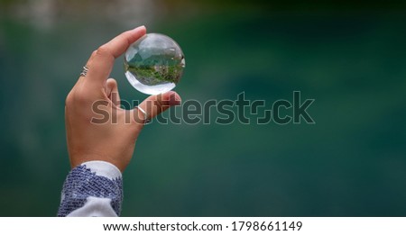 A woman's hand holds a spherical glass ball against the background of a beautiful mountain lake. Turier lake, Alibek glacier, North Caucasus, Dombai,, Russia.