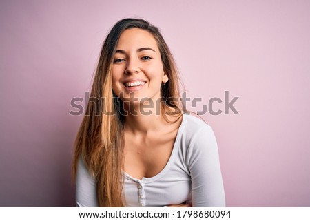 Young beautiful blonde woman with blue eyes wearing white t-shirt over pink background smiling and laughing hard out loud because funny crazy joke with hands on body.