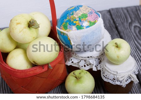 Apples in a red wicker basket. Jam in jars and apples nearby. Fruit harvest. Nearby is a globe with a medical mask.