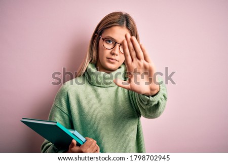 Young beautiful woman wearing glasses holding books over isolated pink background with open hand doing stop sign with serious and confident expression, defense gesture