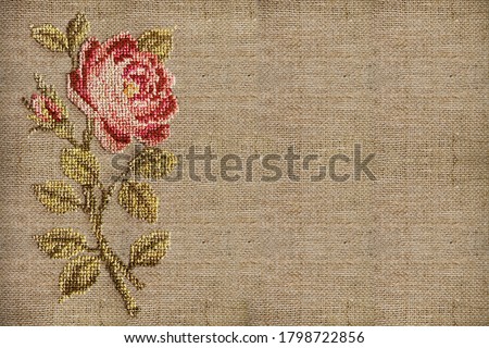 cross-stitched pink rose on a beige fabric background close-up