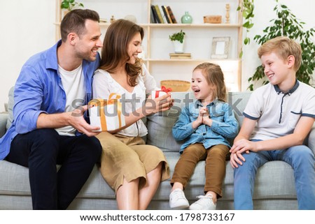 Family Holiday. Happy Parents Congratulating Kids Giving Them Gifts Sitting Together On Couch At Home.