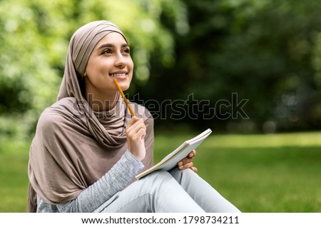 Beautiful girl in hijab writing essay, studying at public park alone, copy space