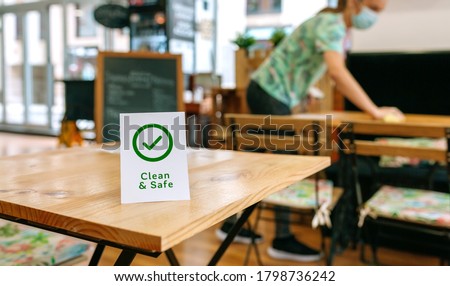Clean and Safe sign placed on a table with waitress cleaning in the background