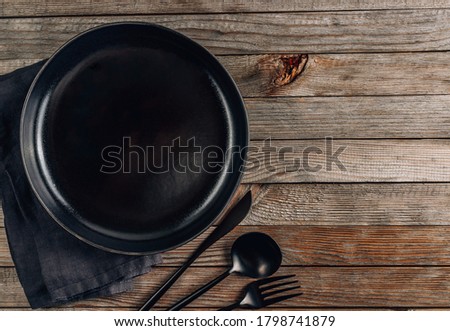 Black plate, cutlery and napkin on rustic wooden background. Table setting. Top view with copy space