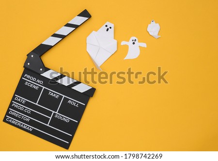Movie Clapperboard and paper ghosts on yellow background. Halloween horror movie. Top view