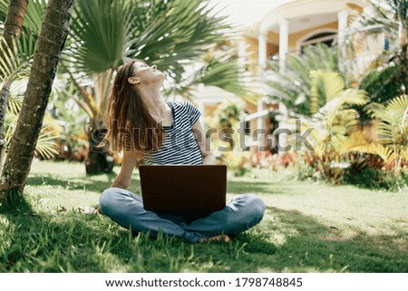 Woman in the park sits on the grass in front of a laptop fresh air companionship