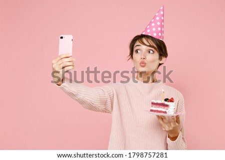 Pretty young woman in casual sweater birthday hat isolated on pastel pink wall background. Birthday holiday party people emotions concept. Celebrating hold cake doing selfie shot on mobile phone