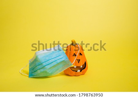 painted pumpkin with a medical mask on a yellow isolated background with space for text