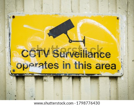 Yellow and black CCTV surveillance sign with white graffiti